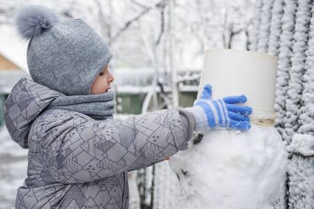 Boy makes a snowman. Adorable kid boy making a snowman, playing and having fun with snow, outdoors on cold day. Active outdoors leisure with children in winterの写真素材