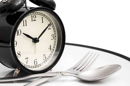 Alarm clock with fork and knife on the plate on white. Time to eat. Healthy food conceptの写真素材