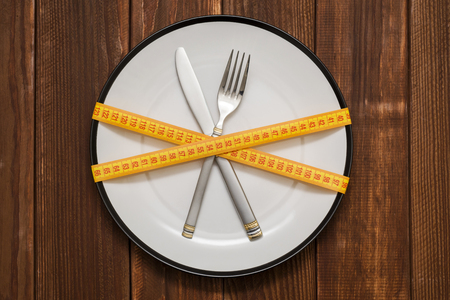 Fork and knife wrapped in measuring tape. Plate with a knife and fork wrapped in measuring tape on a wooden. Healthy eating or dieting concept. Diet conceptの写真素材