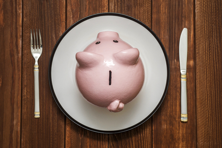 A pink piggy bank on dish. Savings consumer concept. Piggy bank on the plate with fork and knife. Financial conceptの写真素材