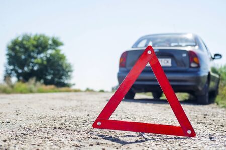 Red warning triangle with a broken down car. Red emergency stop sign and broken car on the roadの写真素材