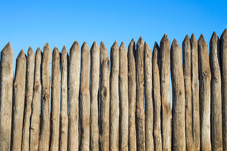 Fence made of sharp wooden stakes against the blue sky. Wooden fence vertical logs pointed against the sky protection against invaders and wild animalsの写真素材