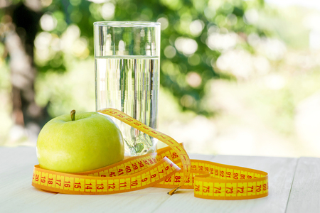 Diet. A apple with water and measuring tape on a white wooden table on green natural background. Health care concept. Healthy lifestyle conceptの写真素材
