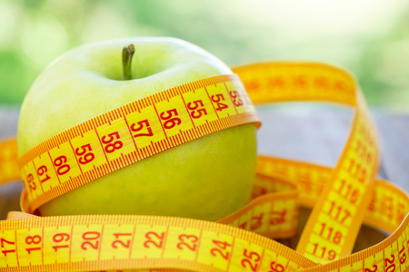 Green apple with measuring tape on wooden background. Apples and sewing tape measure on a wooden table. To lose weight and eat a low calorie apple to lose weightの写真素材
