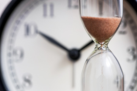 Hourglass on the background of office watch as time passing concept for business deadline, urgency and running out of time. Sand clock, business time management conceptの写真素材