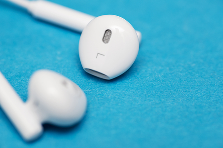 Closeup of white earphones on blue background. Music is my life concept. Earphons on blue background. Trendy colorful photoの写真素材
