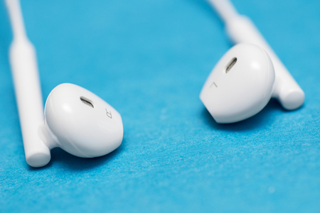 Closeup of white earphones on blue background. Music is my life concept. Earphons on blue background. Trendy colorful photoの写真素材