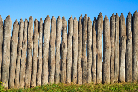 Fence made of sharp wooden stakes against the blue sky. Wooden fence vertical logs pointed against the sky protection against invaders and wild animals. Ancient stockadeの写真素材
