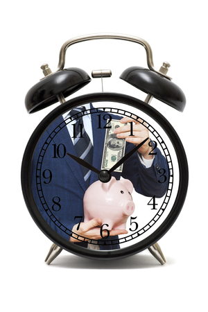 The dial of the alarm clock with the image of a businessman investing money in the piggy bank. Financial long term saving money concept. Time to savings moneyの写真素材