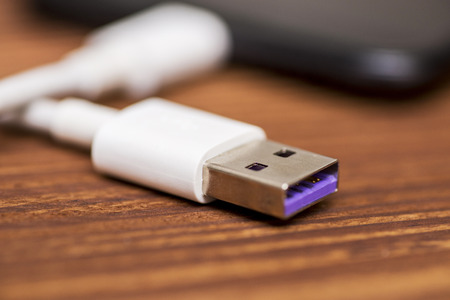 Smartphone with USB cable on the wooden table. Smartphone or tablet with USB cable prepared for data transfer or battery chargingの写真素材