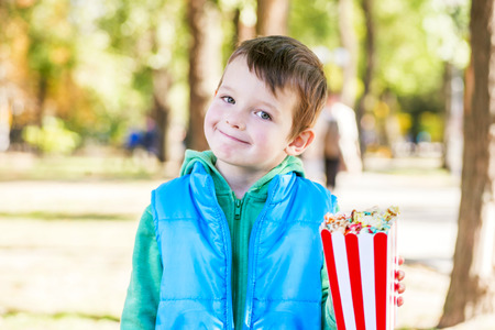 Smiling child with a bucket of popcorn in hand walks in the parkの写真素材