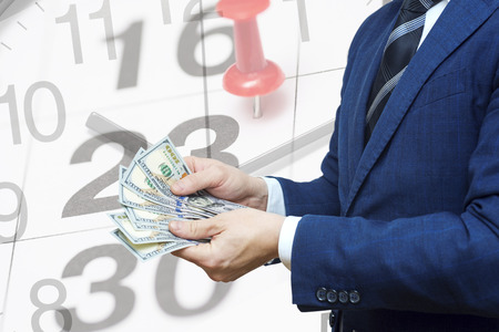 Businessman with money in hand against the background of a calendar with a date stamp pin and arrows of the clock. Tax payment business financial concept. Taxes pay management plan scheduleの写真素材