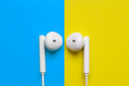 Earbuds or earphones on colorful background. White headphones on a yellow and blue background, top viewの写真素材