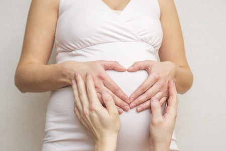 Parents hands making a heart on the belly of the pregnant mother. Pregnant woman and her husband holding her hands in a heart shape on her baby bumpの写真素材