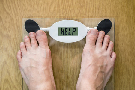 Feet on a bathroom scale with the word HELP on the screen. Lose weight concept with person on a scale measuring kilogramsの写真素材