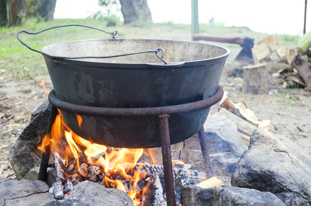 Large metal pot with a lid and handle on tripod used for cooking. Cooking in a bowler hat on the fire in natureの写真素材