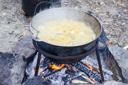 Large metal pot with a lid and handle on tripod used for cooking. Cooking in a bowler hat on the fire in natureの写真素材