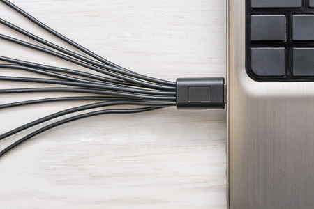 Black USB cables connected to laptop on white wooden backgroundの写真素材