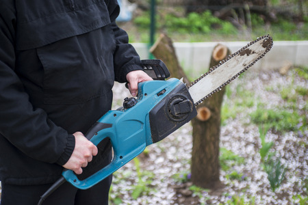 Man in black clothes hold blue chainsaw with his bare hands.の写真素材