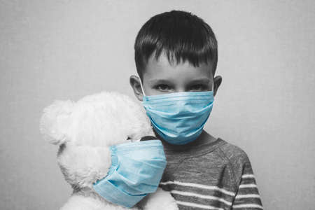 A sad child holds his teddy bear, both wearing protective medical masks. Coronavirus quarantine. Prevention epidemic.の写真素材
