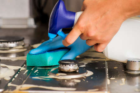 Female hand cleaning gas stove using sponge and detergents. Cleaning a gas stove with kitchen...