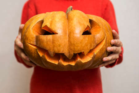 Halloween. Carved orange pumpkin on kid hands, jack-o-lantern traditional symbol of Halloween. Child is holding in his hands carved halloween pumpkin.の写真素材
