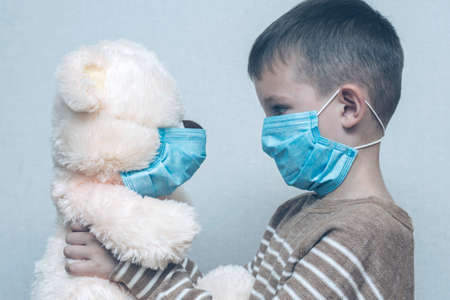 A sad child holds his teddy bear, both wearing protective medical masks. Coronavirus quarantine. Prevention epidemic.の写真素材