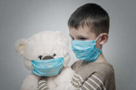 A sad child holds his teddy bear, both wearing protective medical masks. Coronavirus quarantine. Prevention epidemic.の写真素材