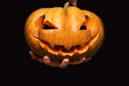 Hand shows halloween pumpkin from darkness. Jack-o-lantern on mans hand on black background. Happy Halloween banner.の写真素材