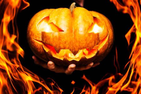 Fire around Halloween pumpkin with burning eyes and mouth in a mans hand. Hand shows burning halloween pumpkin through flames. Happy Halloween banner.の写真素材