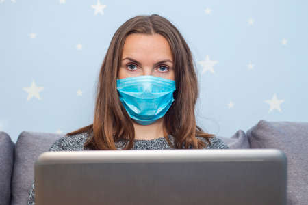 Young business woman in medical mask working from home with laptop during self-isolation and quarantine. Coronavirus outbreak and covid epidemic. Stay home.の写真素材