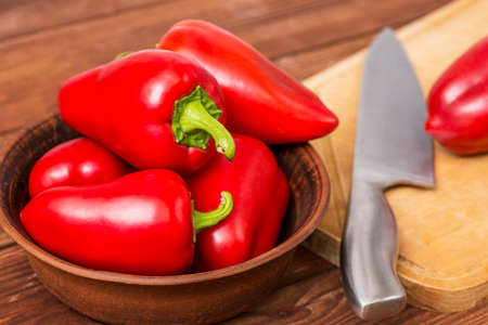 Red sweet pepper in the plate on the table with wooden chopping board and knife. Fresh food. Healthy lifestyle.の写真素材