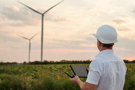 Engineer is checking energy production on wind turbine. Worker in windmills park in helmet and with tablet.の写真素材