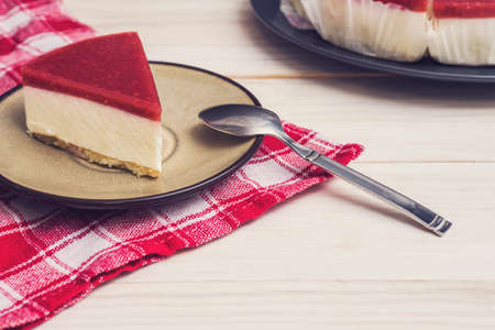 Piece of cheesecake with raspberry jelly on ceramic plate with tea spoon.の写真素材