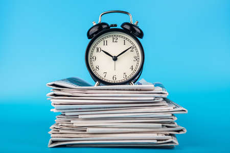 Newspapers and clock on blue background. Retro alarm clock on morning newspapers.