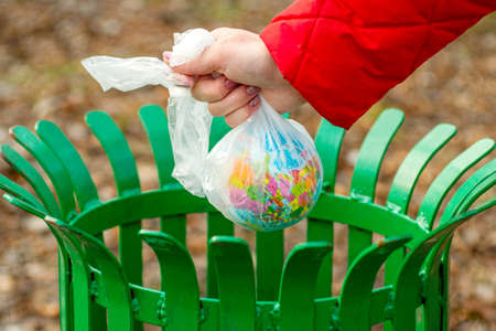 The human hand holds the planet earth in a plastic bag above the trash can. Hand putting Earth globe in trash bin. The concept of Earth Day. Ecology and environment concept.の写真素材