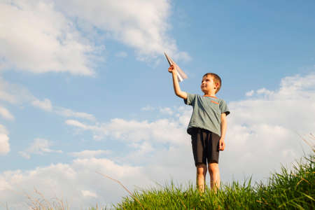 Little boy launches a paper plane into the air. Child launches a paper plane. Happy kid playing with...