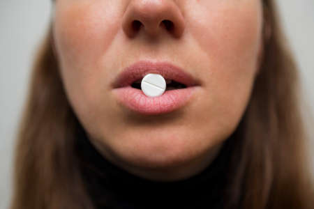 Womans lips hold a large white round pill. Healthcare concept with medicines. Woman taking a tablet from headache or painkiller or abortion pill. Shallow depth of field.の写真素材