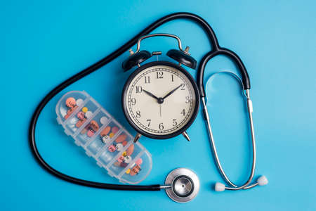 Composition with medical stethoscope, alarm clock and pills on a blue background. Top view. Medical concept.の写真素材