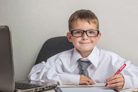 An adorable child is writing on a clipboard in suit and glasses. Little boss in the office. Children pretend to be adults.の写真素材