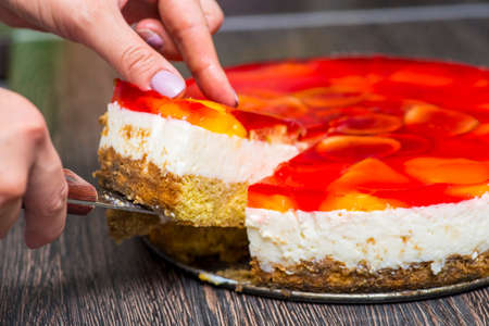 Woman cuts with knife homemade cheesecake on plate on wooden table. The cheesecake is cut with a large kitchen knife.の写真素材