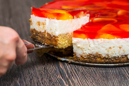 Woman cuts with knife homemade cheesecake on plate on wooden table. The cheesecake is cut with a large kitchen knife.の写真素材