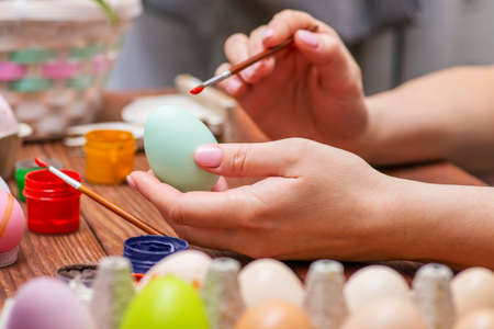 A woman with a tassel paints Easter eggs. Preparing decorations for Easter, creativity with children, traditional symbols. Preparing for Easter.の写真素材