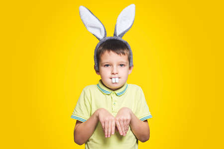 Little boy is acting as a little easter bunny on yellow background. A child is wearing bunny ears and teeth on Easter day.の写真素材