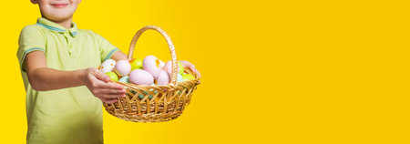 Little child is holding basket with painted eggs on yellow background. Easter day.の写真素材