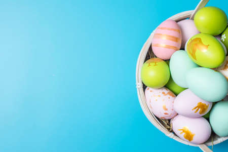 Easter basket filled with painted Easter Eggs over a blue background. Colorful painted easter eggs in basket on blue background.の写真素材
