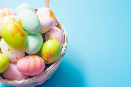 Easter basket filled with painted Easter Eggs over a blue background. Colorful painted easter eggs in basket on blue background.の写真素材