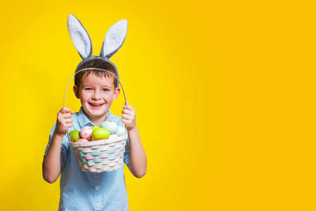 Cute little child wearing bunny ears on Easter day and holding basket with painted eggs. Happy kid is holding Easter basket.の写真素材