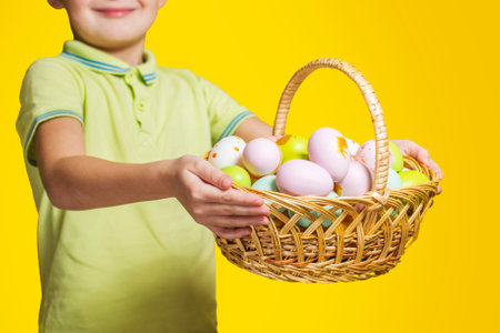 Little child is holding basket with painted eggs on yellow background. Easter day.の写真素材