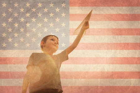 Little boy launches a paper plane into the air on the flag of america background. Child launches a paper plane with pride.の写真素材